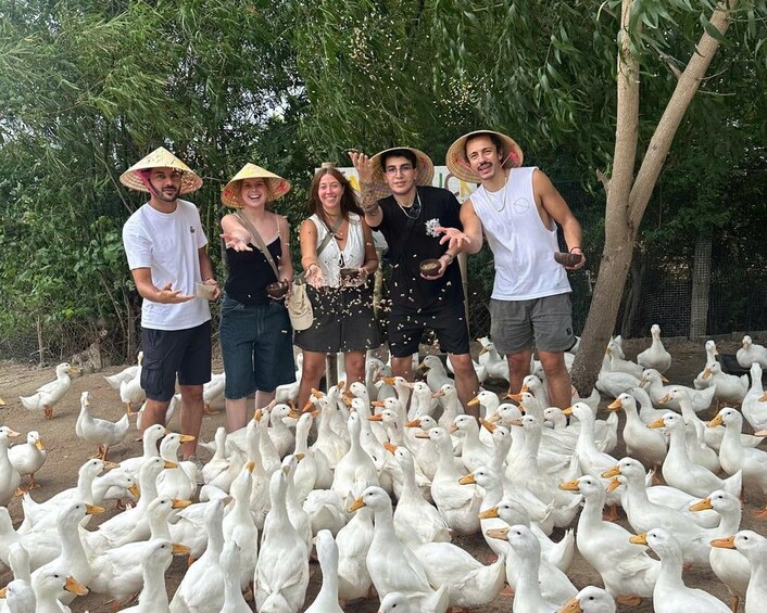 A group of people standing in a field with a flock of white ducks. 1