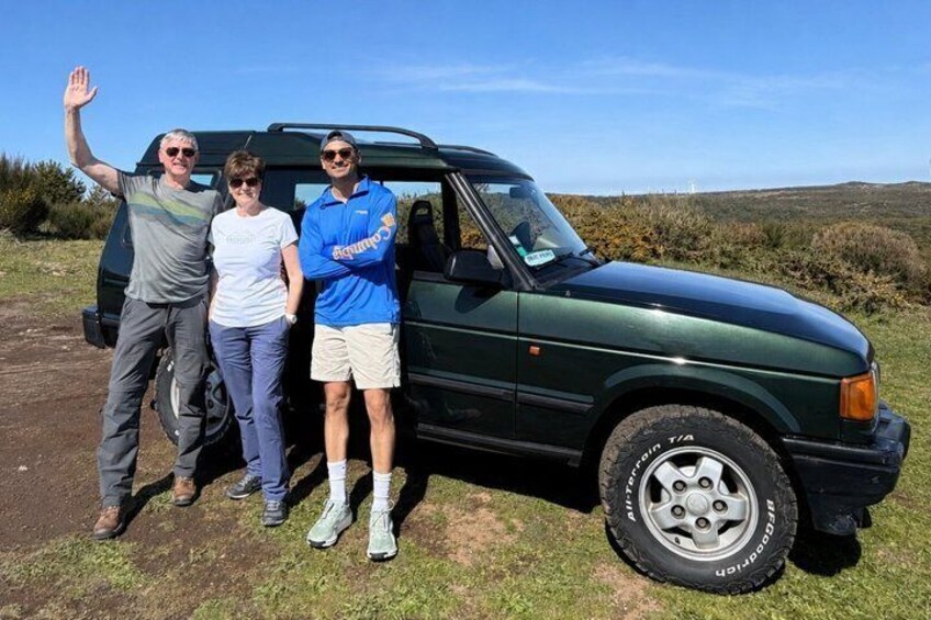 Three people standing next to a green SUV on a grassy field with a clear sky. 5