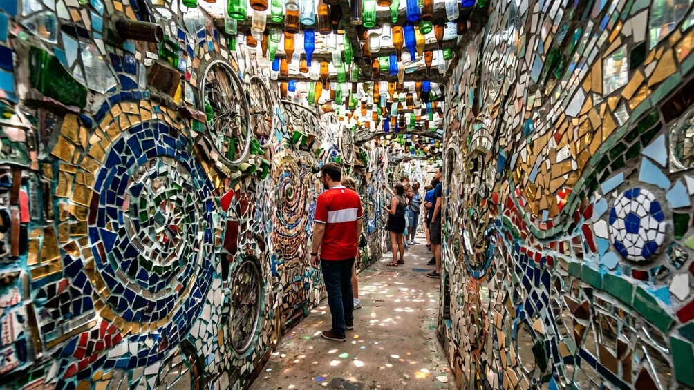 A narrow alleyway lined with colorful mosaic walls and hanging glass bottles. 4