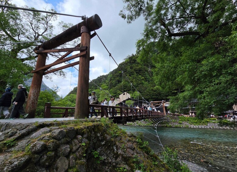 A suspension bridge over a river with a wooden structure and a stone wall in the foreground. 3