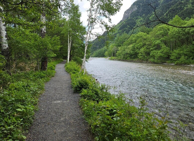 A gravel path beside a river, surrounded by lush greenery and a mountain backdrop. 2