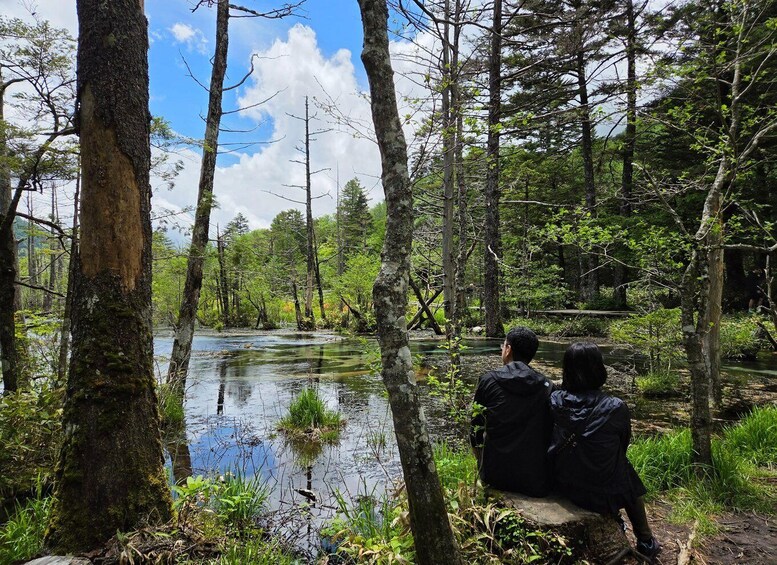 Two people sitting on a bench overlooking a forested river. 1