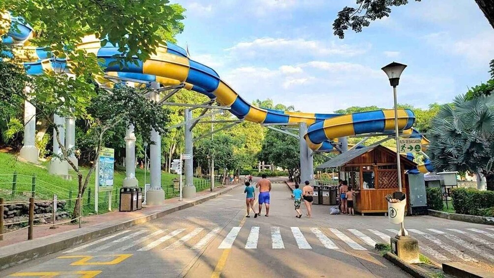 A water park entrance with a blue and yellow slide, a pedestrian crossing, and a small wooden structure. 4