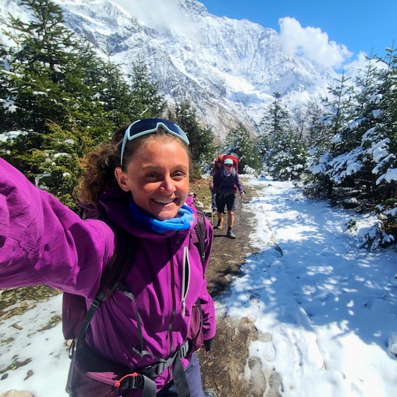A person in a purple jacket taking a selfie on a snowy mountain trail with another hiker in the background. 2