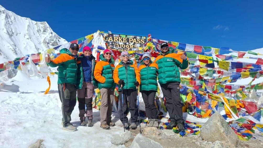 A group of people at the base of a mountain with a sign reading 'LARKE PASS 5100M'. 1