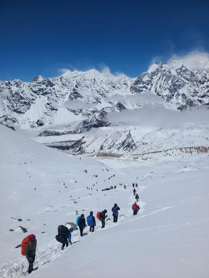 A group of hikers ascending a snow-covered mountain slope with a clear sky and snow-capped peaks in the background. 3