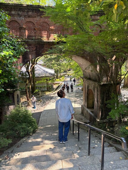 A stone pathway leading through a park with a brick archway and a traditional tiled-roof structure in the background. 3