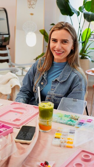 A person sitting at a table with a drink, crafting supplies, and a pink tray. 2