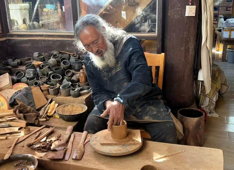 A person working with pottery on a wheel, surrounded by various clay items and tools. 1