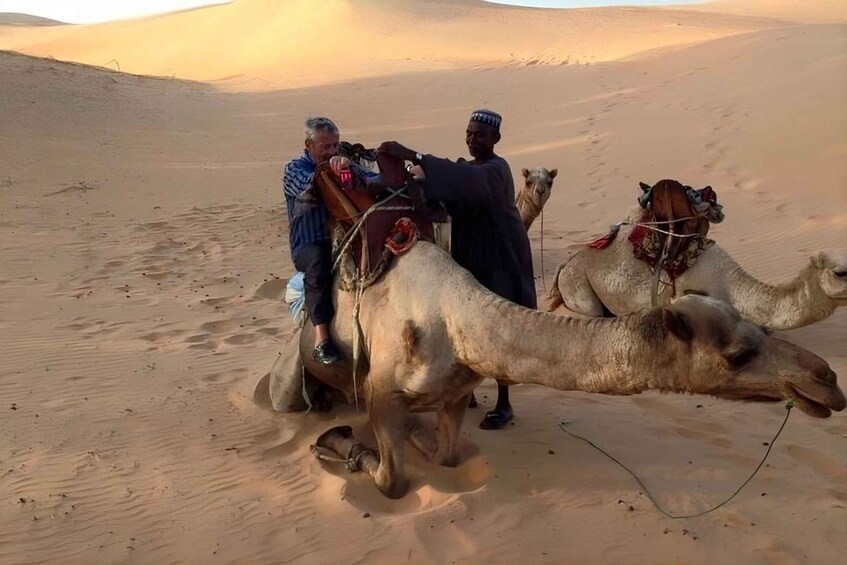 Two camels with riders in a desert landscape. 2