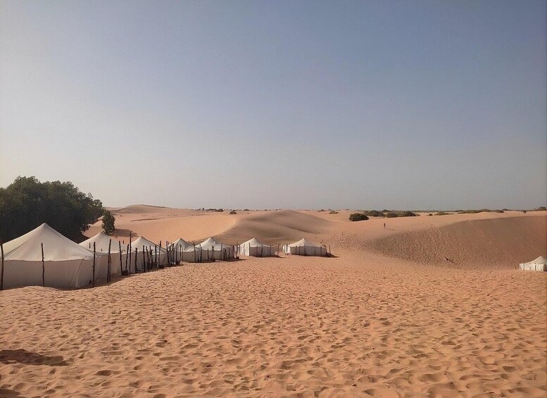 A desert landscape with sand dunes and white tents. 1