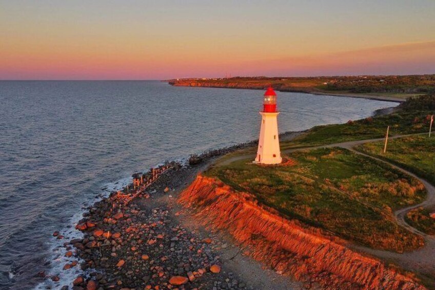 A lighthouse on a rocky coastline at sunset. 1
