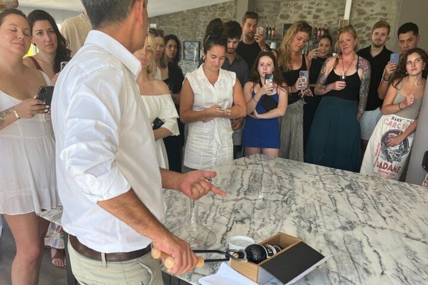 A man in a white shirt presenting at a marble table with a crowd of people around. 2