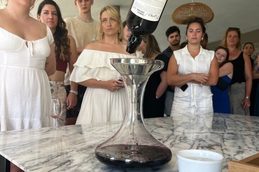 A group of people observing a wine decanter on a marble table. 4