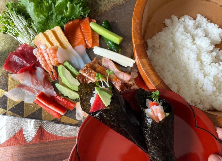 A variety of sushi and sashimi on a wooden tray, with a bowl of white rice beside it. 1