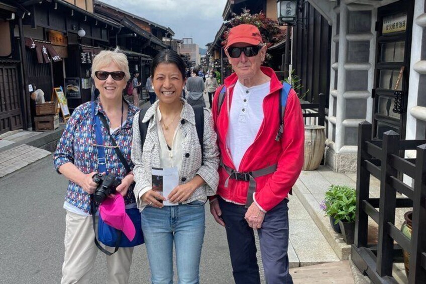 Three people standing on a street with shops and a traditional building in the background. 5