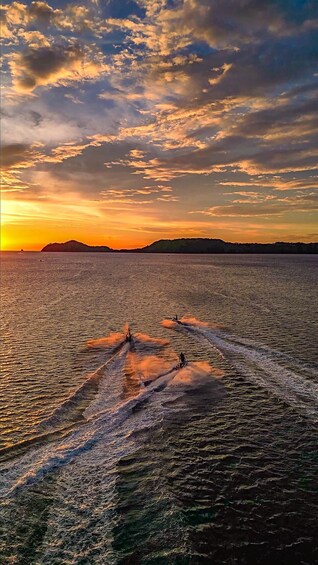 Un barco avanza rápidamente sobre el agua al atardecer, con un paisaje montañoso al fondo. 2