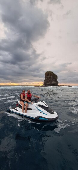 Una persona conduciendo un jet ski sobre el agua, con una isla rocosa al fondo. 1
