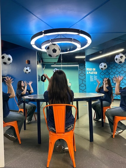 A group of people seated at a table in a room with blue walls and hanging soccer balls. 4