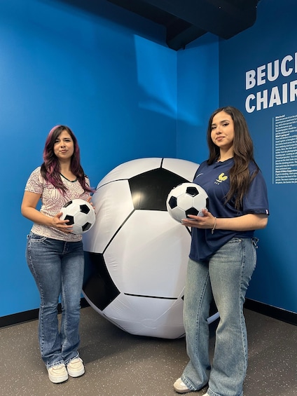 Two people holding soccer balls in front of a blue wall with a large soccer ball and the text 'BEUCCHAIR'. 2