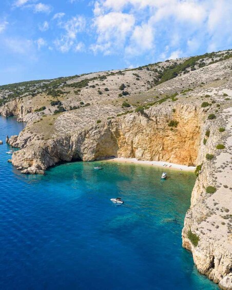 A coastal landscape with clear blue waters, rocky cliffs, and a sandy beach. 5
