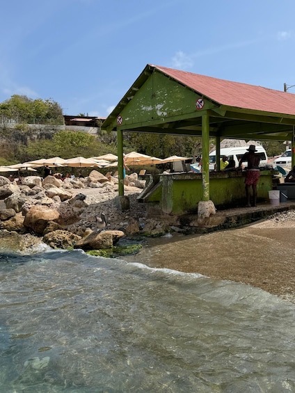 A rocky beach with a green shelter, clear water, and people near the shore. 3