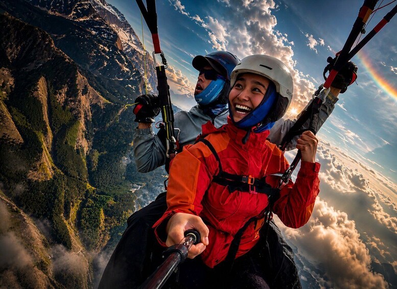 Two individuals paragliding over a mountainous landscape with a rainbow. 1