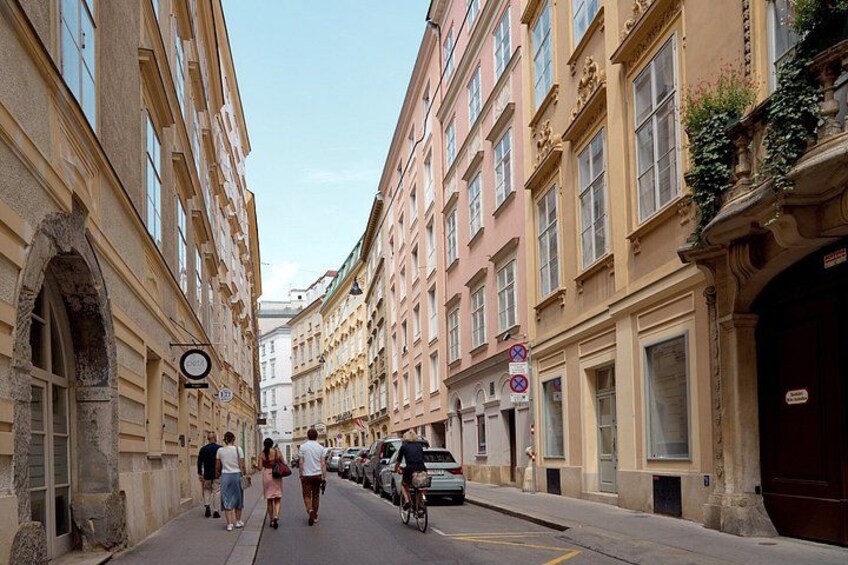 A narrow street flanked by historic buildings, a bicycle, and pedestrians. 3