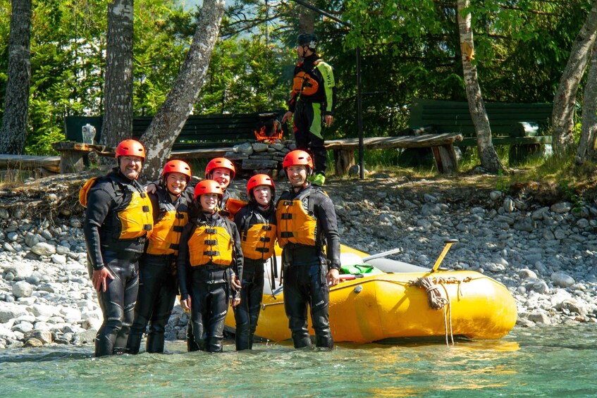 A group of people in wetsuits and helmets standing by a yellow raft on a riverbank. 5