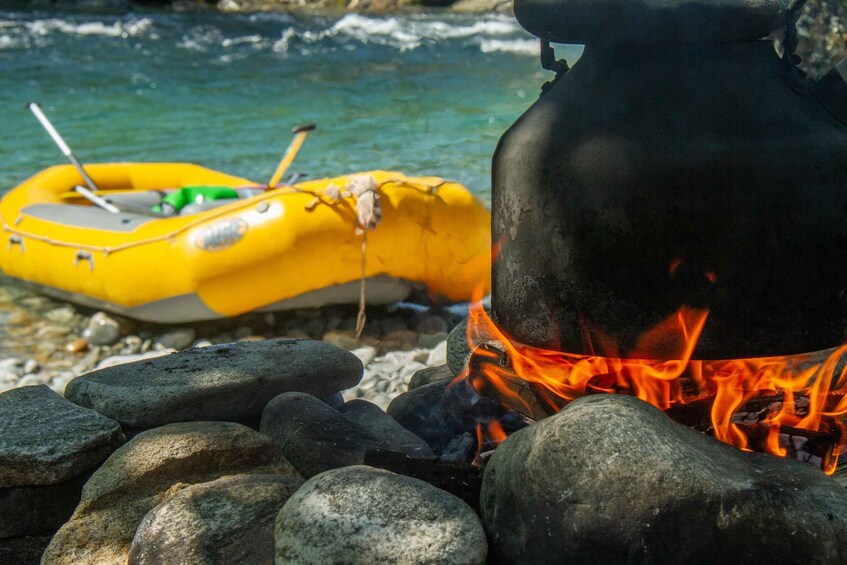 A campfire with rocks, a yellow raft, and a river in the background. 2