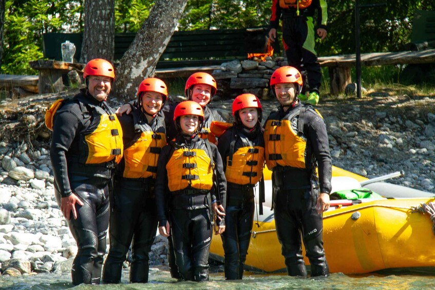 A group of people in wetsuits and helmets standing by a yellow raft. 4