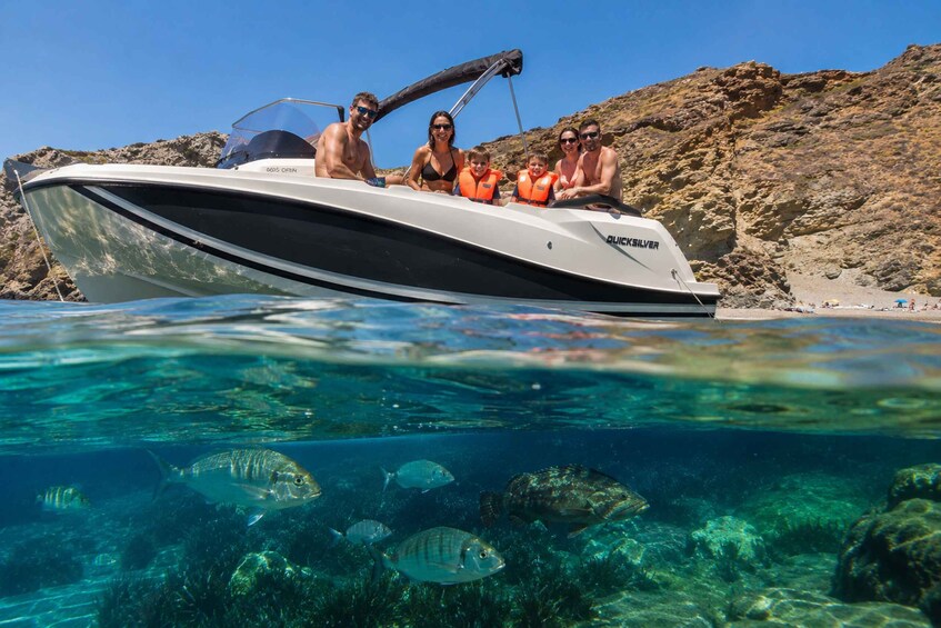 A boat with people on it, clear water, and rocky shoreline. 1