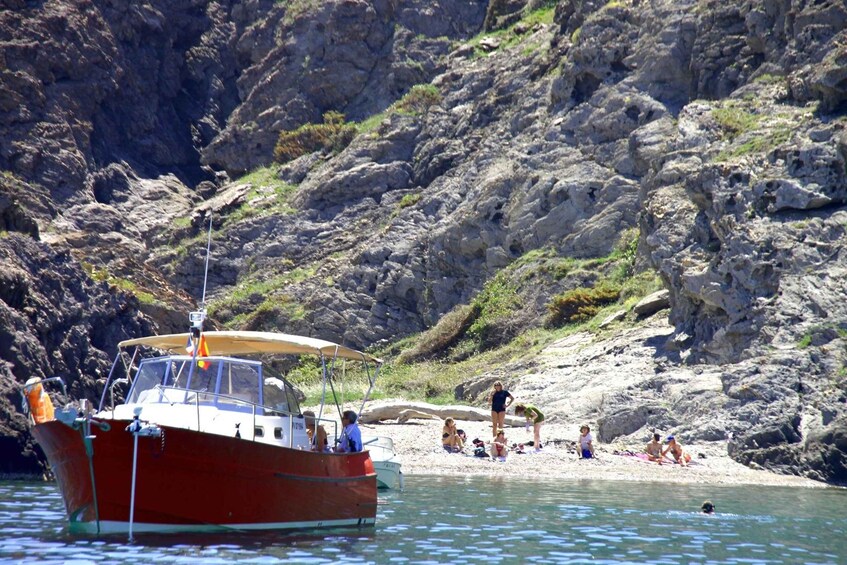 A red boat anchored near a rocky beach with people sunbathing and swimming. 5