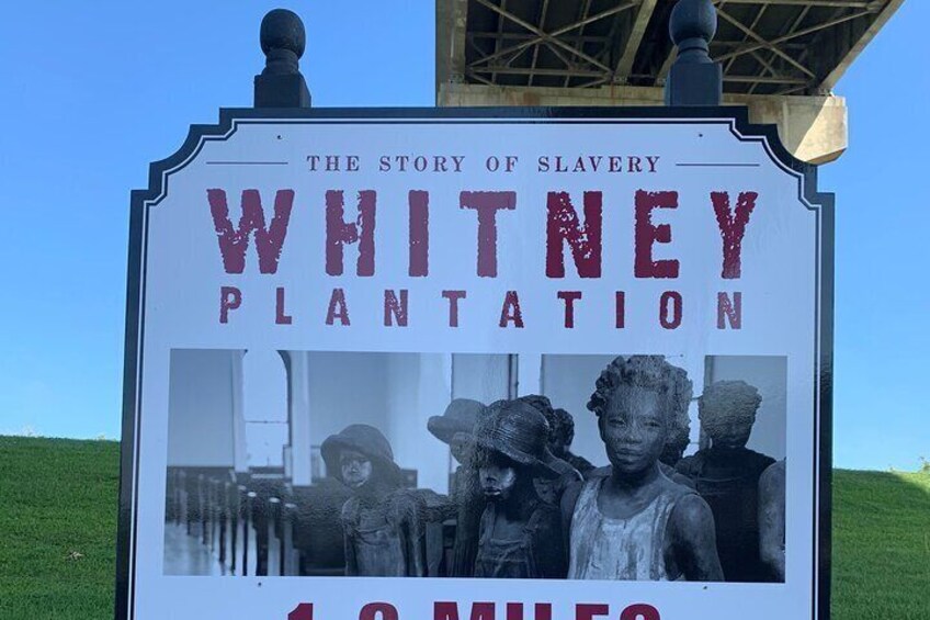 Un panneau d’information sur la plantation de Whitney, qui relate l’histoire de l’esclavage et indique une distance de 1,6 kilomètre (1,0 mille). 1