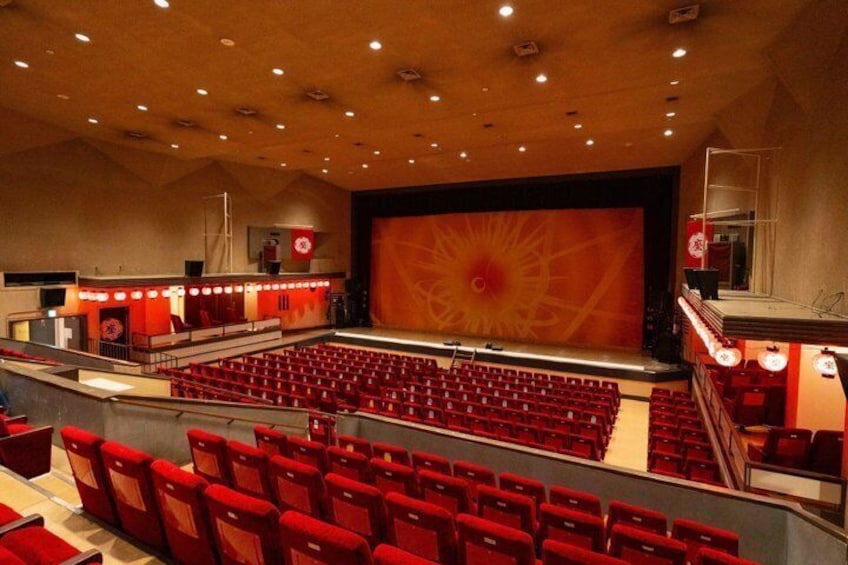 A theater with red seats, a large stage, and a red and yellow abstract design on the backdrop. 3