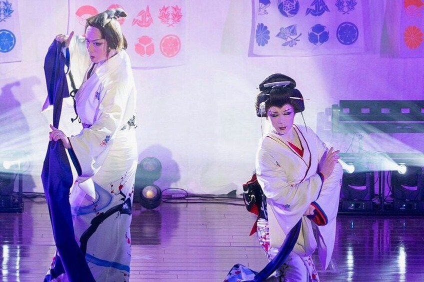 Two performers in traditional Japanese attire on a stage with a backdrop of cultural symbols. 2