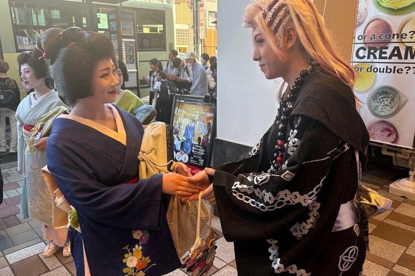 Two people in traditional attire, one handing over a bag to the other. 2