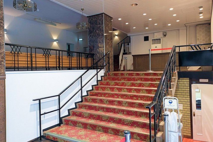 A staircase with red carpeted steps, a black railing, and a white wall with a door. 4