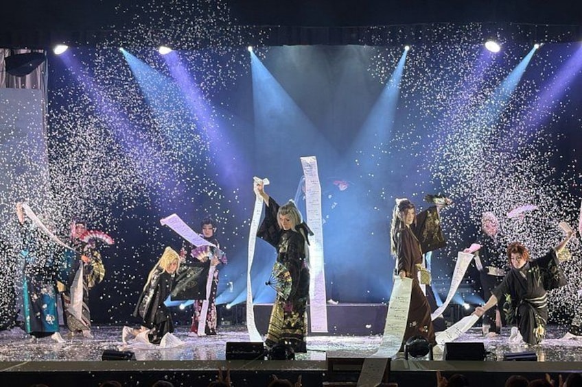 A stage with performers in traditional attire, confetti, and stage lights. 1