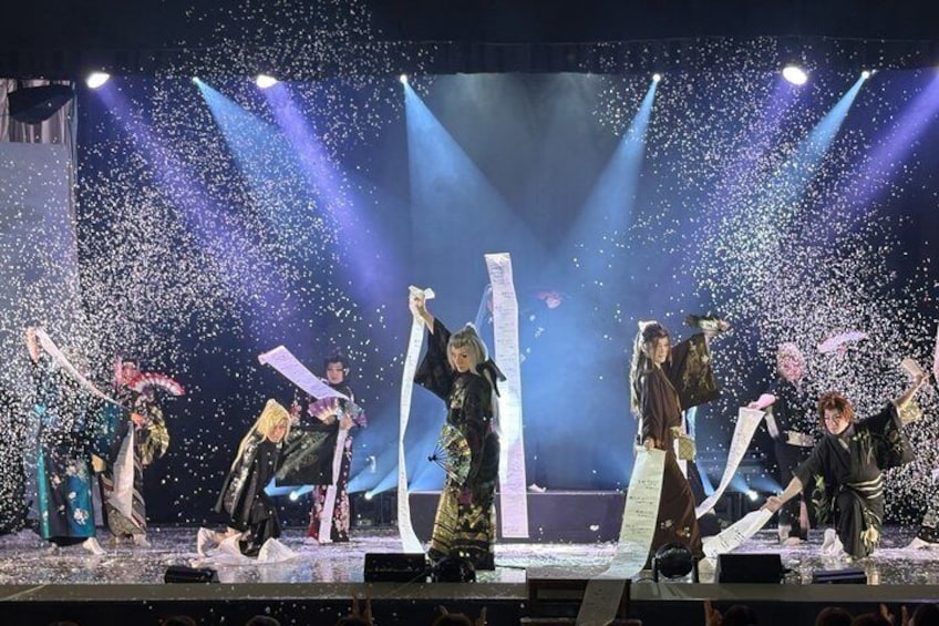 A stage performance with performers in traditional costumes, confetti, and stage lighting. 1