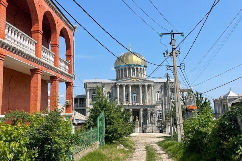 A large building with a dome, a red brick structure, and a green fence. 3