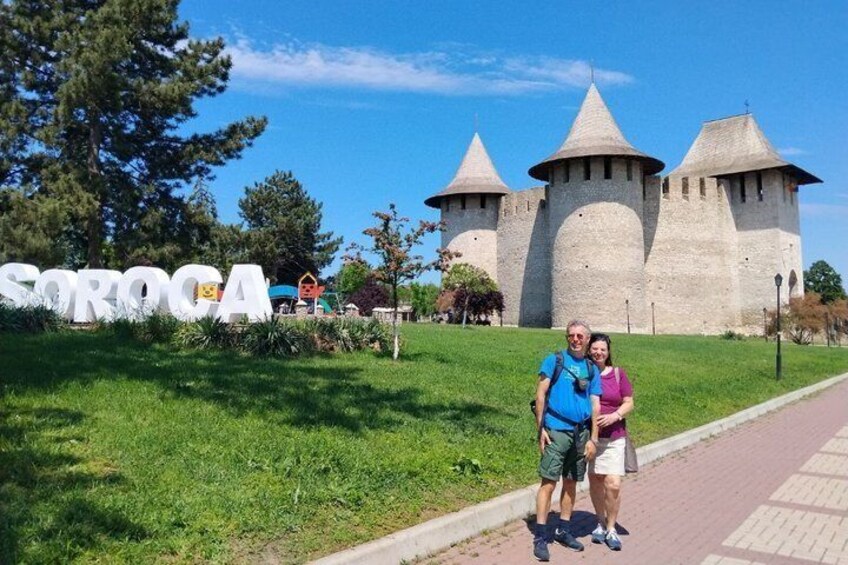 A castle with three towers, a sign reading 'SOROCSA,' and a grassy area with two people standing. 1