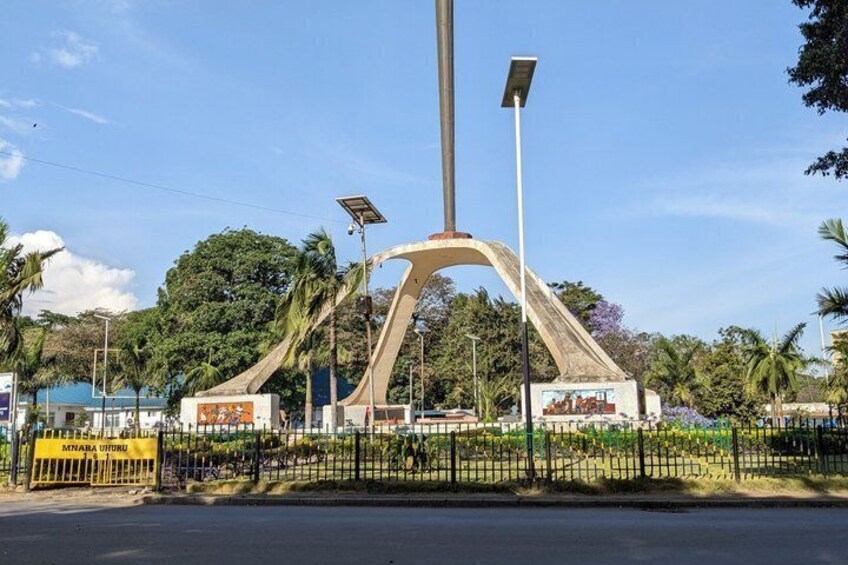 A large, modern sculpture with a curved design, surrounded by a fence and palm trees. 3