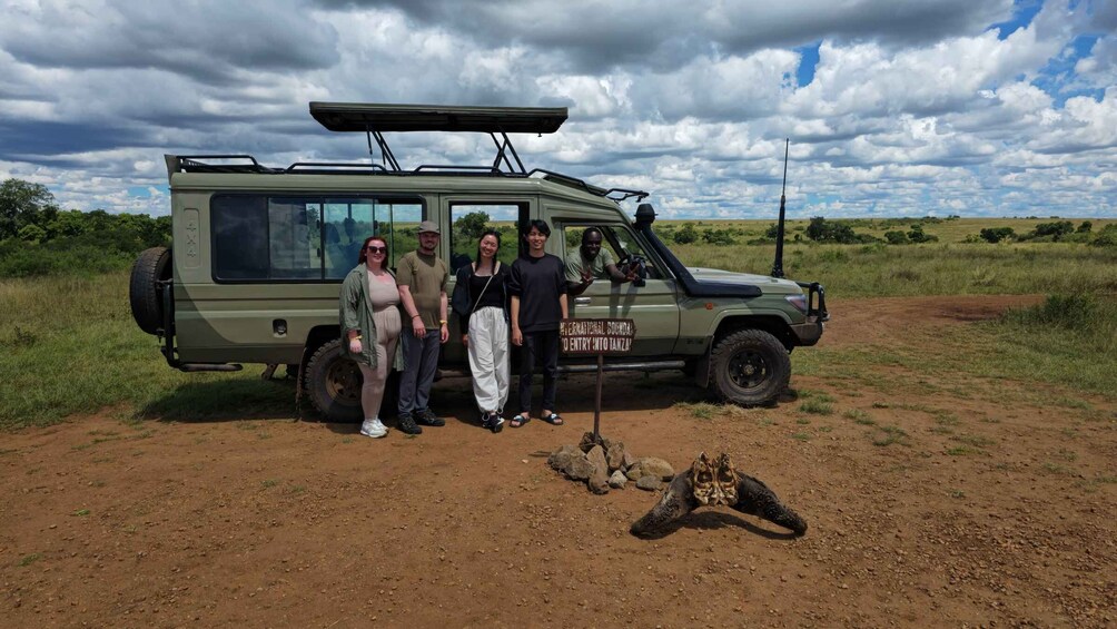 A group of people posing in front of a safari vehicle with a sign indicating entry into Tanzania. 4