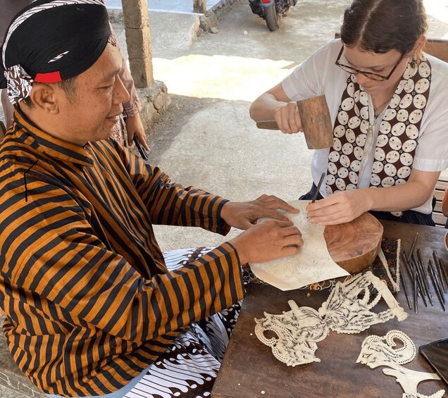 Two people engaged in a craft activity, possibly making traditional items, with tools and materials scattered on a table. 2