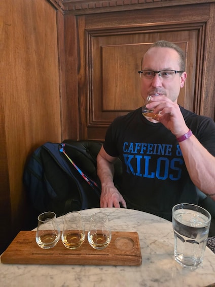 A person sitting at a table with three glasses of a golden liquid and a glass of water. 3