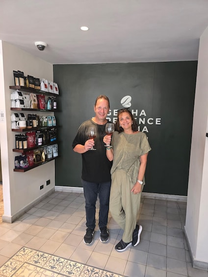 Two people standing in a room with a wall displaying coffee bags and a logo. 2