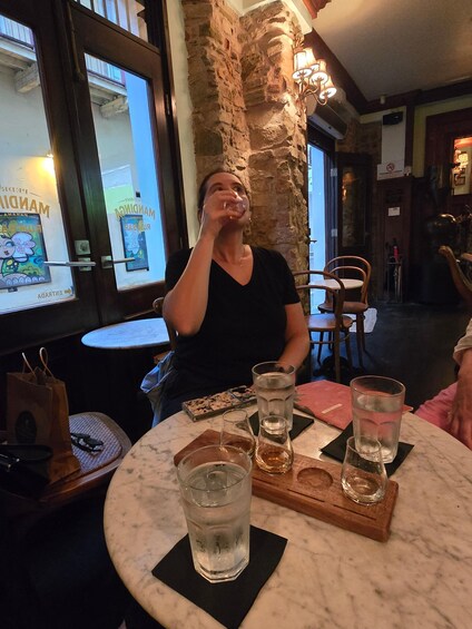 A person sitting at a table with a drink, in a restaurant with stone walls and a view of the street outside. 2
