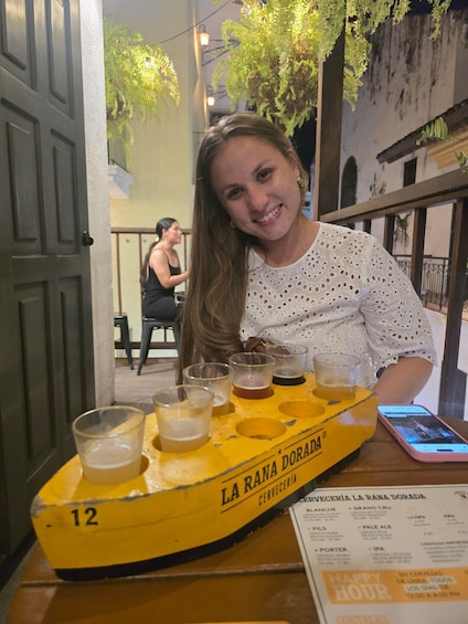A person seated at a table with a yellow beer tap labeled 'LA RANA DORADA' and a menu with various beer options. 5