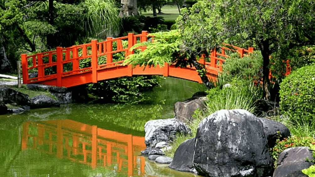 A red bridge over a pond with rocks and greenery. 1